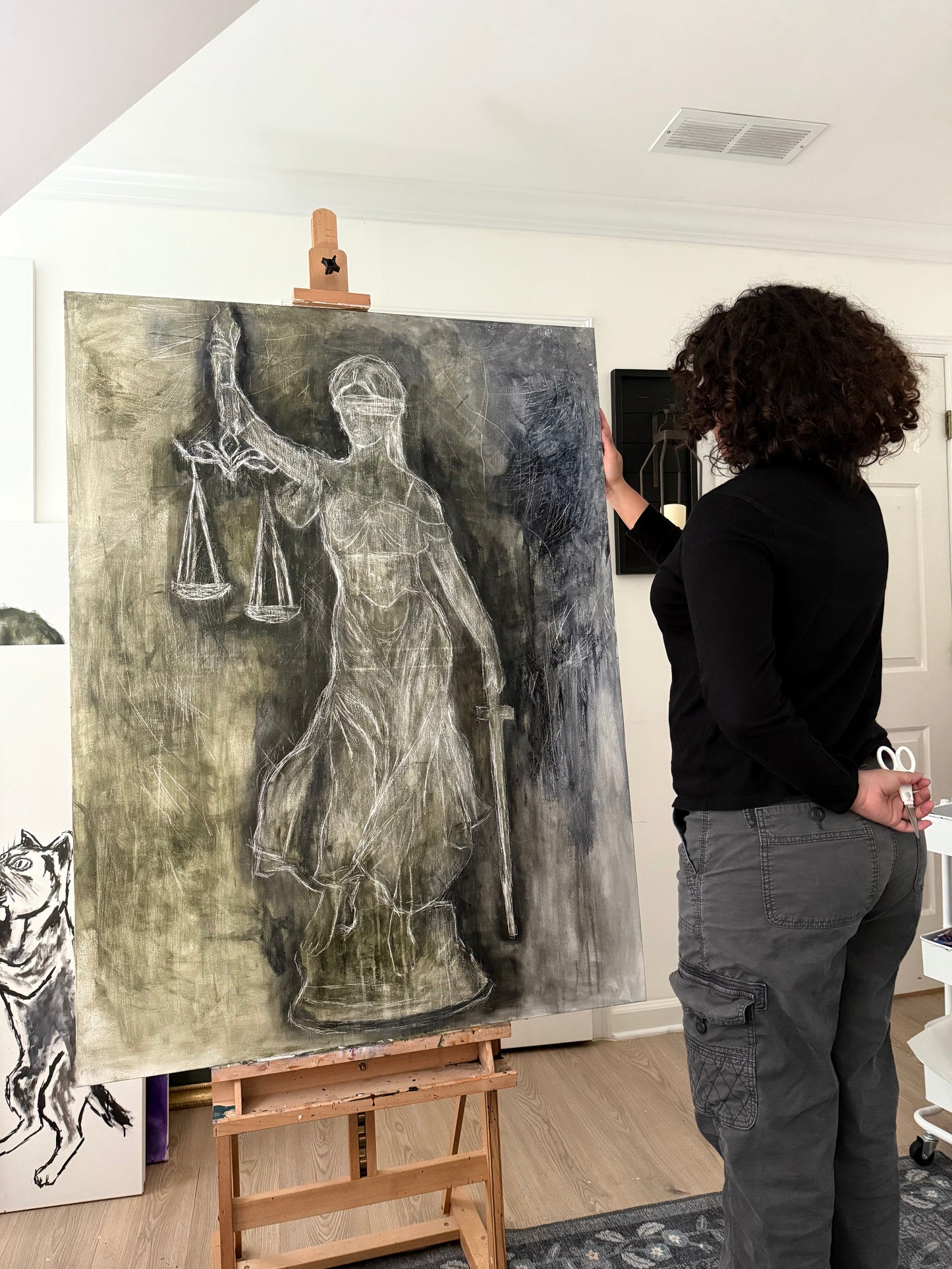 Person standing next to a large artwork of a classical statue on an easel in an art studio.